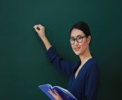 young teacher with blue notebook writes on chalkboard.jpg from teacher