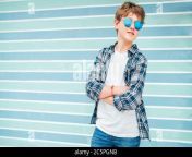 fashion portrait of caucasian blonde hair 12 year old teenager boy dressed t shirt and checkered shirt in blue sunglasses posing on turquoise blue bac 2c5pgnb.jpg from 12 old blonde tee